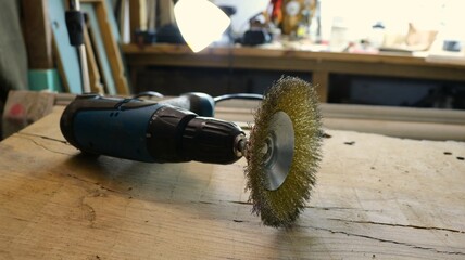 A manual device for grinding a tree on a workbench as an industrial still life, a working tool with a round bristled metal brush lying on a wooden surface in a workshop