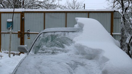 part of a gray car half buried in a thick layer of snow and half cleared of a snowdrift, a passenger vehicle in a private yard in the process of clearing a large snow drift after a winter storm