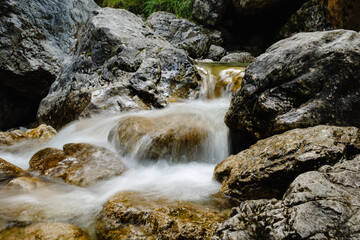 Naklejka na ściany i meble Mountain River Flowing Over Rocks with Blurred Motion and Lush Green Surroundings