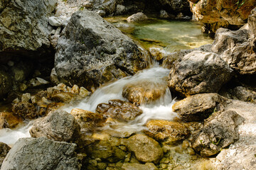 Naklejka na ściany i meble Mountain waterfall with sunlit boulders and lush greenery, serene and captivating.