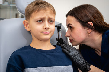 little boy, fair-haired teenager, sitting in an otolaryngologist's office, having an ear examination at the doctor's, worried, emotional, but smiling. Physical examination