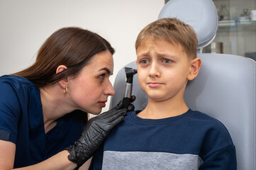 little boy, fair-haired teenager, sitting in an otolaryngologist's office, having an ear examination at the doctor's, worried, emotional, but smiling. Physical examination