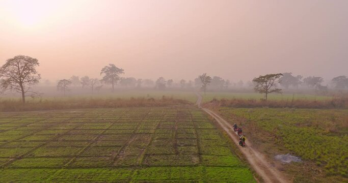 Terai region Nepal traveling trails drone shot three motorbike riders travels enjoying the scenic beauty of plain land cultivable greenery harvest, trees adds beauty to golden hour sunset 4K