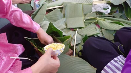 A woman's hand pours beans into a leaves to prepare to wrap Banh Chung, a traditional Vietnamese cake.