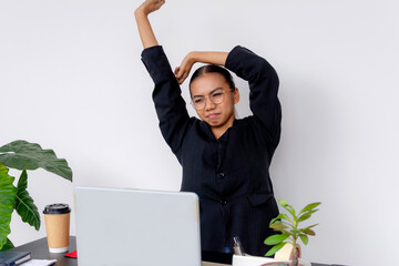 Young professional personal assistant stretching her arms at her desk with a white background and a relaxed expression. - obrazy, fototapety, plakaty