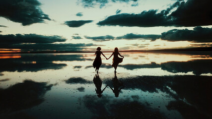 Fototapeta premium A young two woman dance across the mirror like surface of salt lake as the sun disappears behind the clouds.