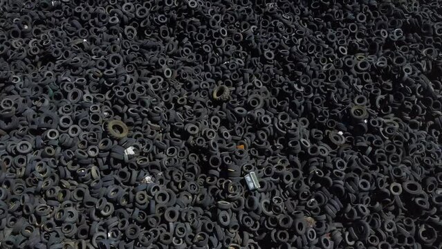 A pile of hundreds of tires gathered together in a landfill shown by a drone aerial shot.