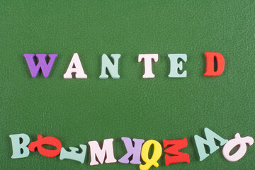 WANTED word on green background composed from colorful abc alphabet block wooden letters, copy space for ad text. Learning english concept.