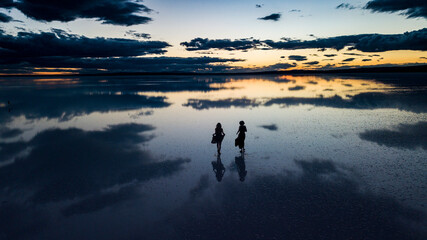 young two woman dance across the mirror like surface of salt lake as the sun disappears behind the...