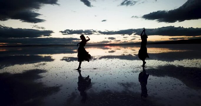  A young two woman dance across the mirror like surface of salt lake as the sun disappears behind the clouds.