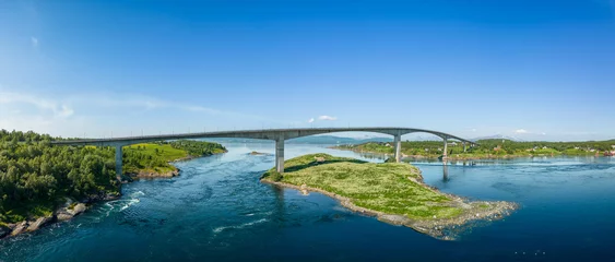 Poster Im Rahmen A panoramic drone shot of Saltstraumen Bridge arching over the world's strongest tidal current, with lush green islets and distant mountains under a clear blue sky © Artem