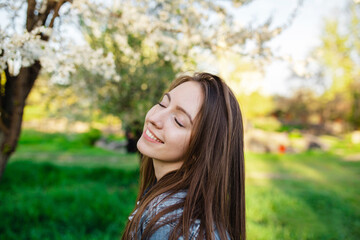 Portrait of a handsome smiling with teeth girl in a spring garden at sunset. A woman relaxes in a park with blooming apple and cherry trees.