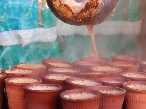 Authentic local and traditional street drink in India and South Asia Chai masala spiced or unspiced tea. Liquid poured from a brewing pot after being strained into multiple terracotta cups.