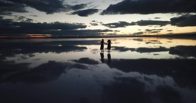  A young two woman dance across the mirror like surface of salt lake as the sun disappears behind the clouds.