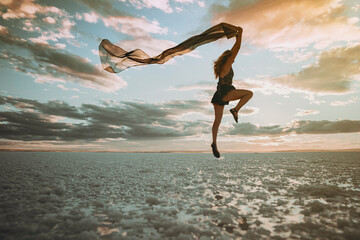 A beautiful woman gracefully dances on the beach by the sea on a summer day, her movements fluid...