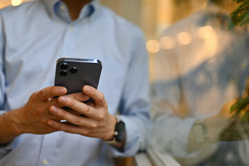 Cropped image with an unrecognizable businessman using a smartphone beside the window