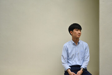 Portrait of a young Asian man sitting on the bottom edge of the image. With space for messages or advertisements