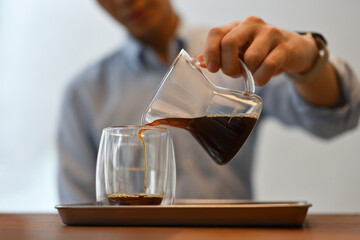 Cropped image of a Young male pouring a coffee into a glass, Focus on the pitcher