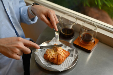 A looking down view of a male's hands using a fork and knife to eat a croissant, Having brunch in the cafe