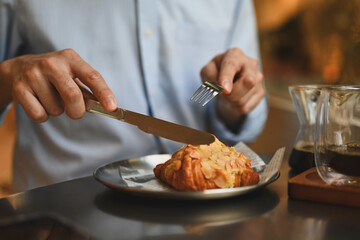 Cropped image of a Young man enjoying a breakfast during using a fork and knife to eat a croissant...