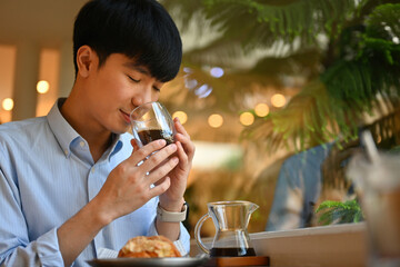 Portrait of a Smart Young Asian Man Feels refreshed by drinking and a cup of coffee and enjoying with croissant