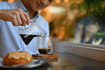 Cropped image of Asian male pouring Freshly brewed coffee from pitcher to empty glass in the cafe