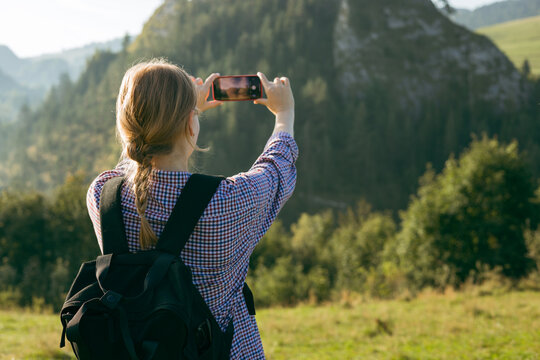 Tourist on top of the mountain takes a photo. Woman traveler takes a photo on a modern smartphone, makes beautiful pictures of beautiful mountain landscapes. Active lifestyle concept, rear view