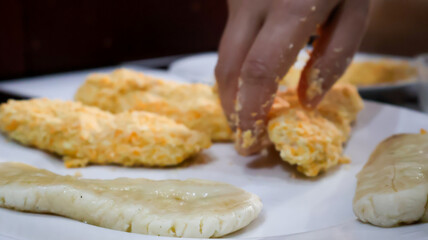 Close-up of a woman making fried banana by coating the banana in golden bread crumb to then be fried. Ideal for food blogs, cooking concepts, food enthusiasts, and cooking-themed designs. 