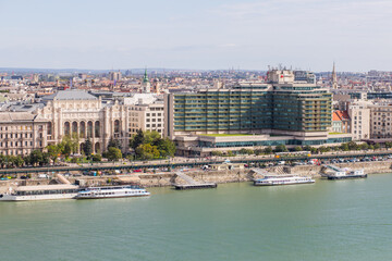 Obraz premium Embankment with several ships and boats. Clear blue water of the river. Modern buildings in a big city. Architecture with columns and glass facade.