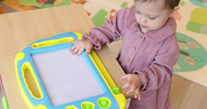 little child girl drawing on magnetic erasable board in her room