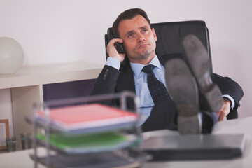 a focused businessman engages in a crucial phone call at the office in a modern workspace. He demonstrates the essence of multitasking and efficiency - 727073825