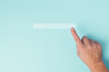A single human hand is captured pointing to a virtual search bar on a plain pastel blue background, symbolizing the action of online searching, digital inquiry and research concept.
