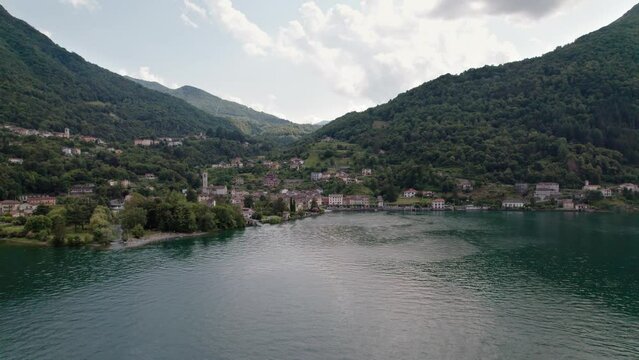 Drone flies over the lake and you can see the small fishing village of Osteno in Italy. Breathtaking scenery on a beautiful summer day. Pan camera movement from left to right