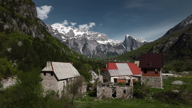 Scenic aerial drone view of village in Theth National Park in Albania with snowy mountains and clouds in the background