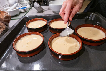 Stockholm, Sweden A woman in a residential kitchen makes Crème Brûlée desserts on the counte in small dishes.