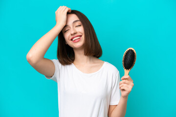 Young ukrainian woman with hair comb isolated on blue background has realized something and...