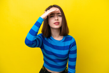 Young Ukrainian woman isolated on yellow background looking far away with hand to look something