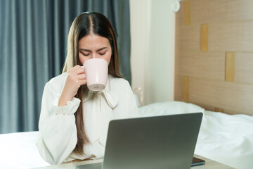 Pensive young woman sips coffee while gazing at her laptop, blending a moment of reflection with productivity. female adult enjoys a cup of coffee during a thoughtful work break on her laptop