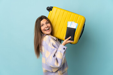 Young Slovak woman isolated on blue background in vacation with suitcase and passport