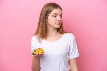 Teenager Russian girl holding a tartlet isolated on pink background looking to the side