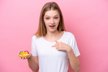 Teenager Russian girl holding a tartlet isolated on pink background with surprise facial expression