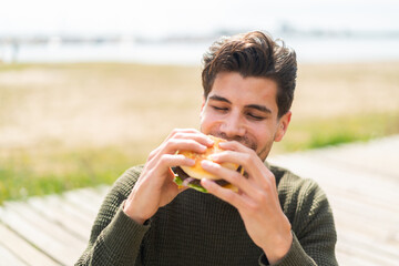 Young caucasian man at outdoors holding a burger