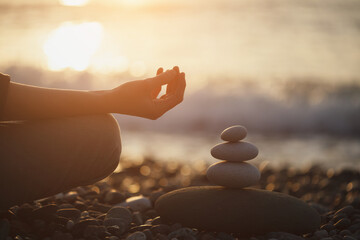 Woman practicing yoga and meditation and pyramid of pebbles on the beach, zen, harmony, spiritual concept, peace of mind