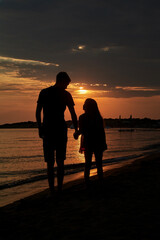 Silhouettes of two people, brother and sister, walking on the beach for sunset time