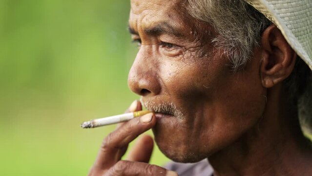Closeup of elderly farmer smoking cigarette in rural asia, weathered face and age lines
