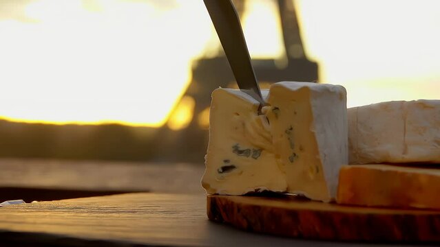 Hands cutsing a piece of Bresse Bleu cheese on a wooden board close-up on a background of the Eiffel Tower