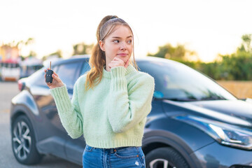 Young pretty girl holding car keys at outdoors thinking an idea and looking side