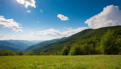 mountainous rural landscape on a sunny afternoon forested hills and green grassy meadows in evening light ridge in the distance sunny weather with fluffy clouds on the bright blue sky