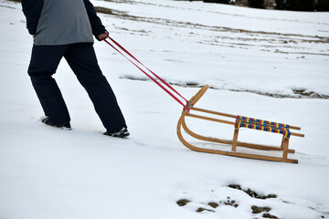 A man pulls a sledge up a hill in the winter tobogganing - obrazy, fototapety, plakaty