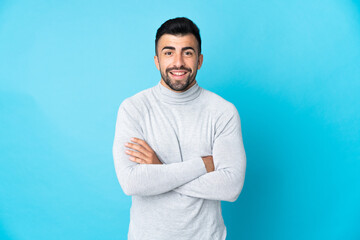 Caucasian man over isolated blue background keeping the arms crossed in frontal position